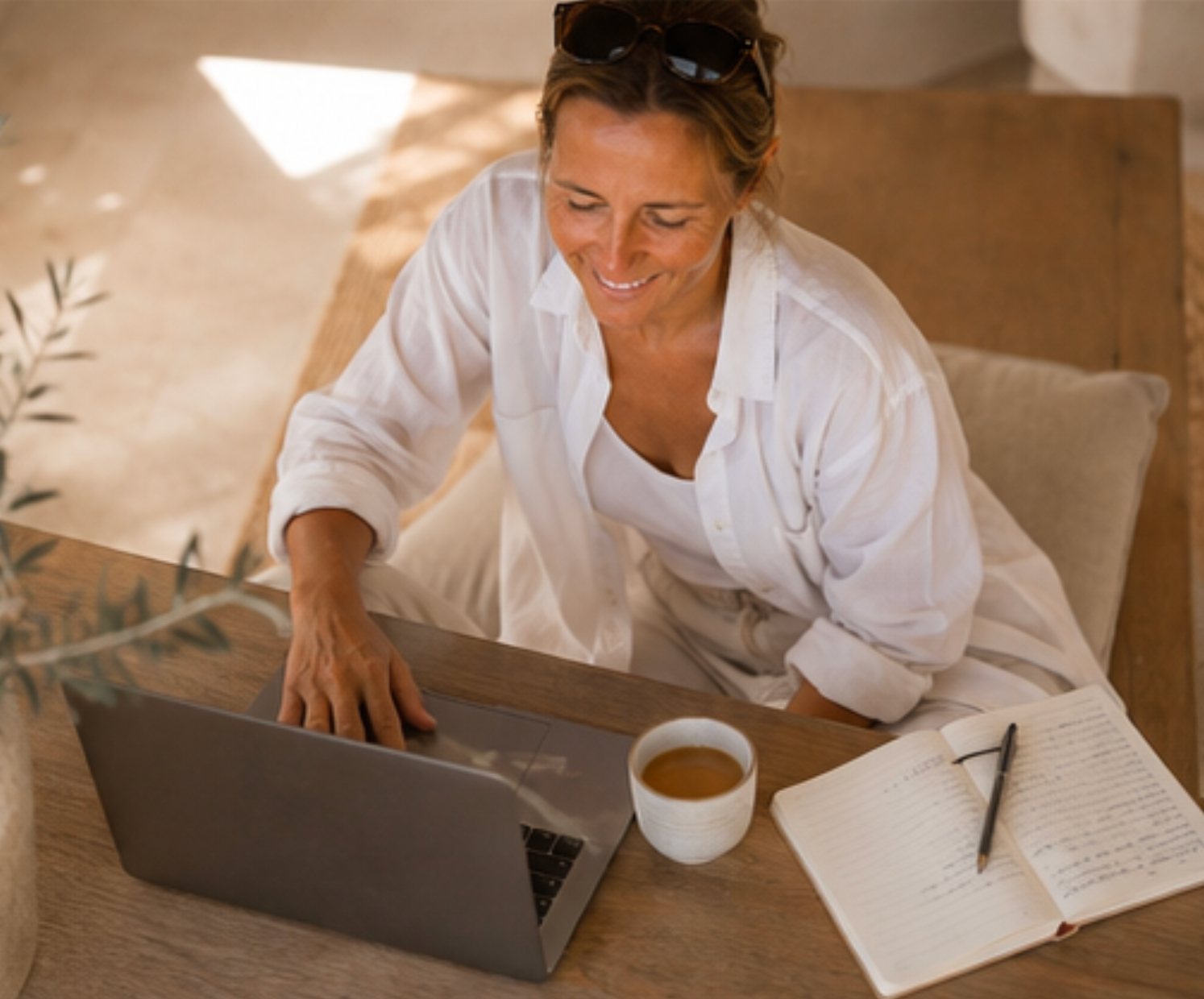 Heidi lächelt am Laptop, mit Notizbuch und Kaffee auf dem Tisch